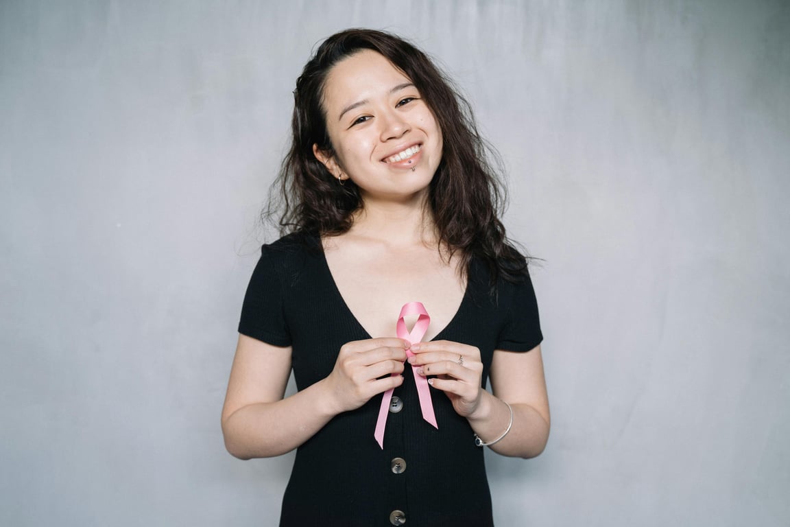 Portrait of a smiling woman holding a pink ribbon symbolizing breast cancer awareness.