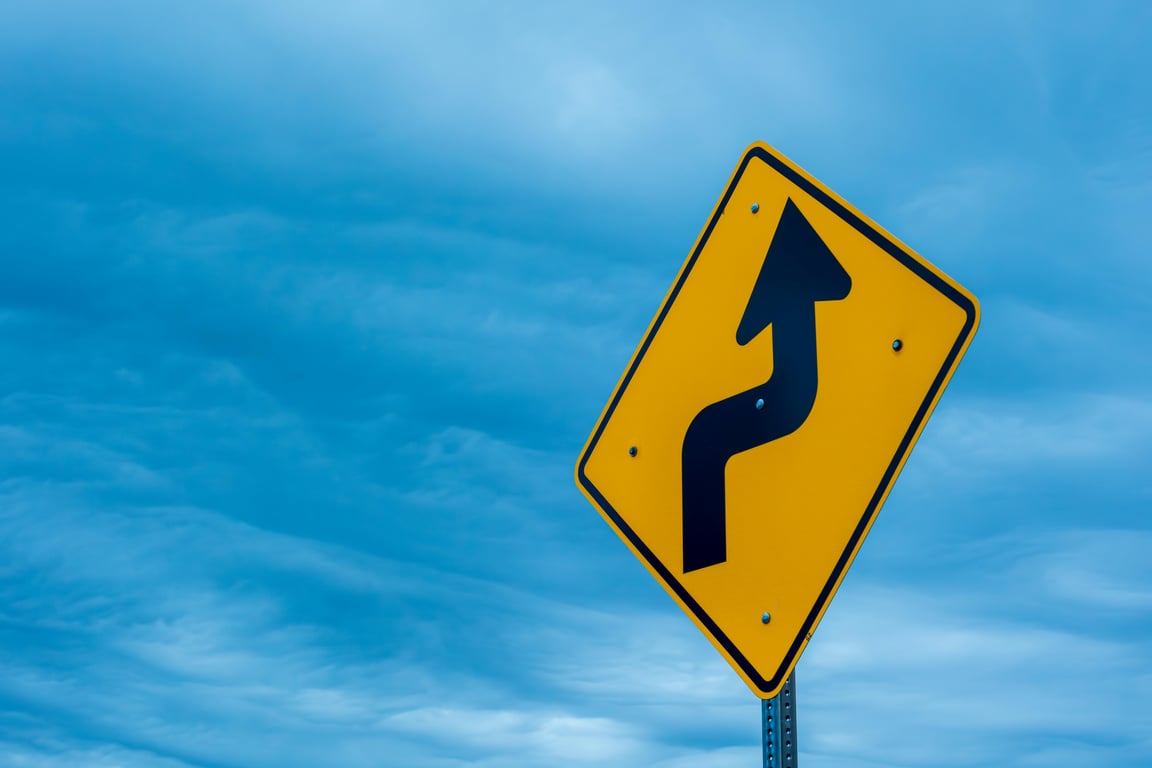 Yellow right turn road sign with blue sky background, symbolizing traffic and safety.