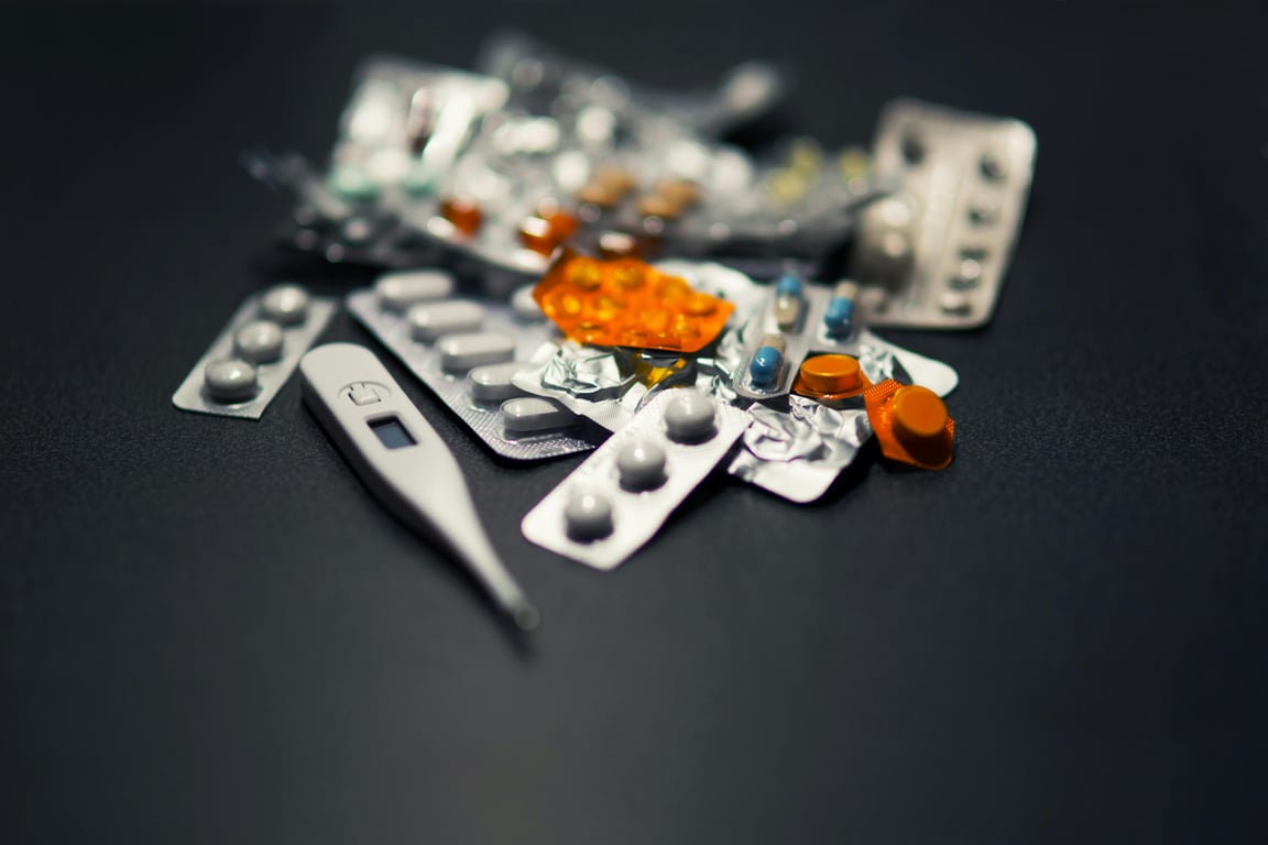 Close-up of various pills and a digital thermometer against a dark background.