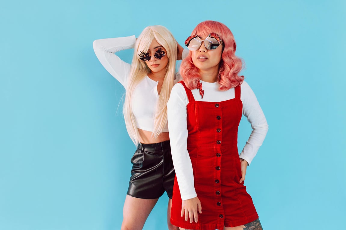 Two fashionable women posing confidently with unique sunglasses against a vibrant blue backdrop.