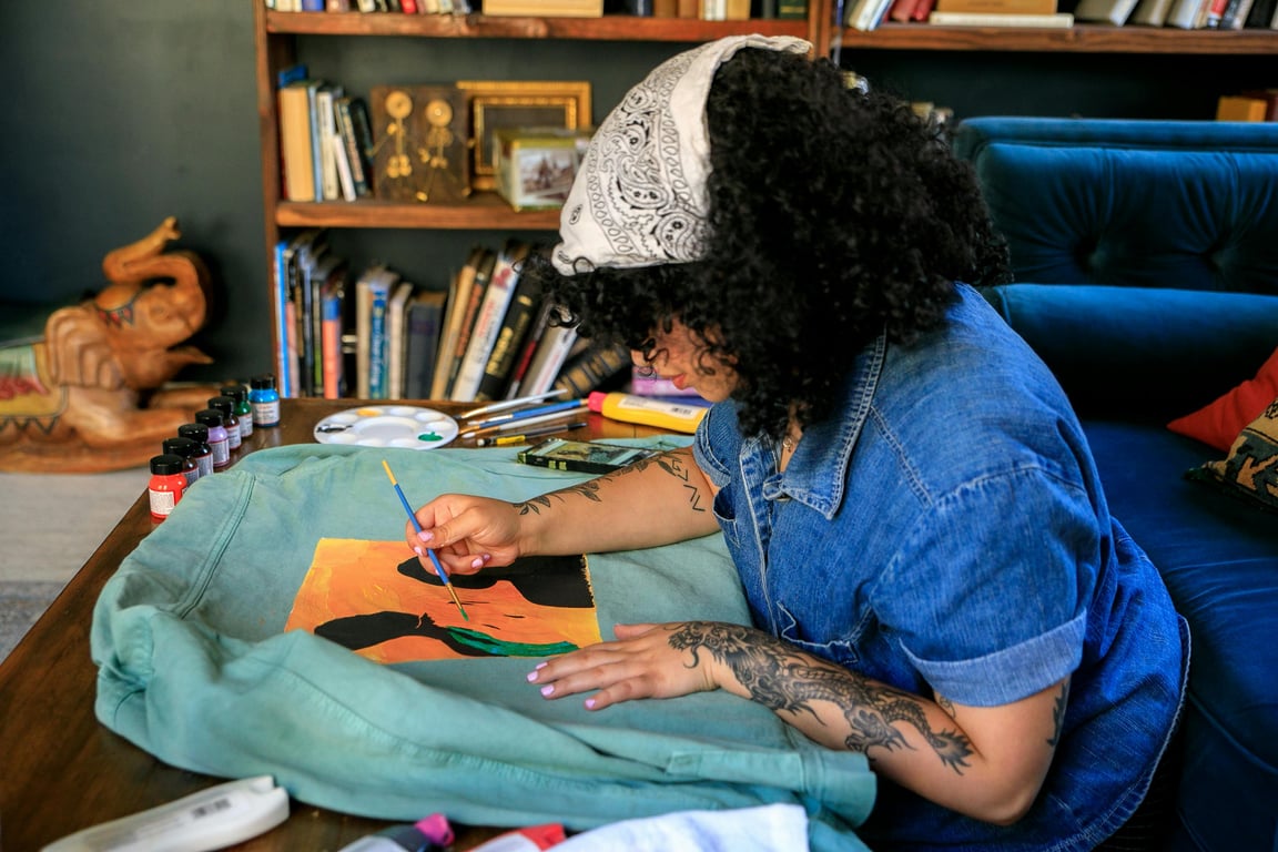 A woman artist paints a vibrant design on fabric indoors, showcasing her skill and creativity.
