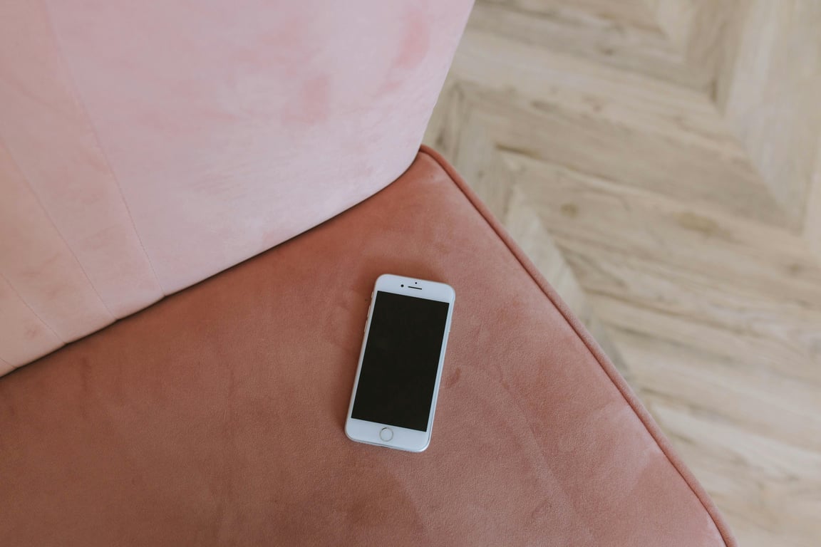 Minimalist composition of a smartphone on a pink couch corner, top view.