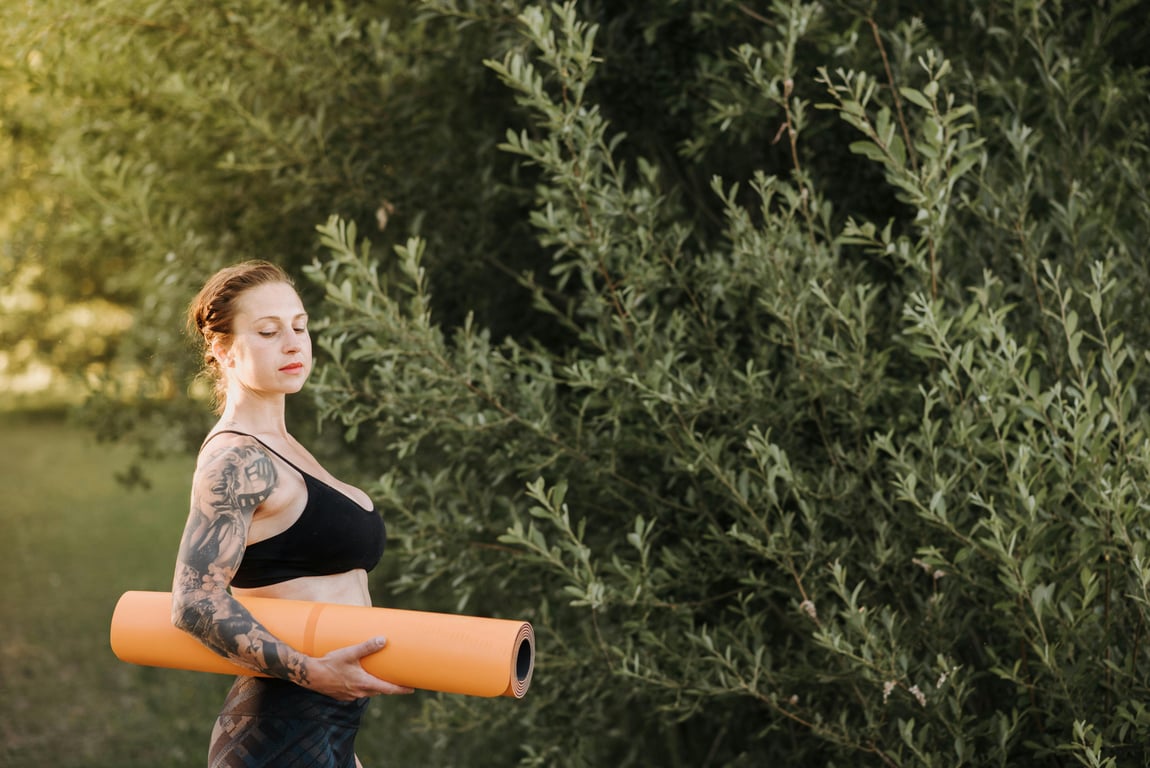 Tranquil scene of a woman with a yoga mat in a peaceful outdoor setting. Embracing nature and wellness.