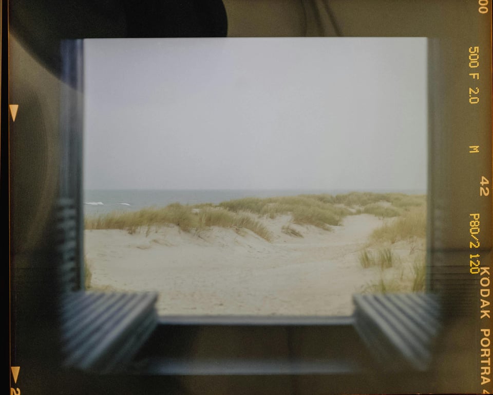 A serene view of a sandy beach and ocean framed by a window.