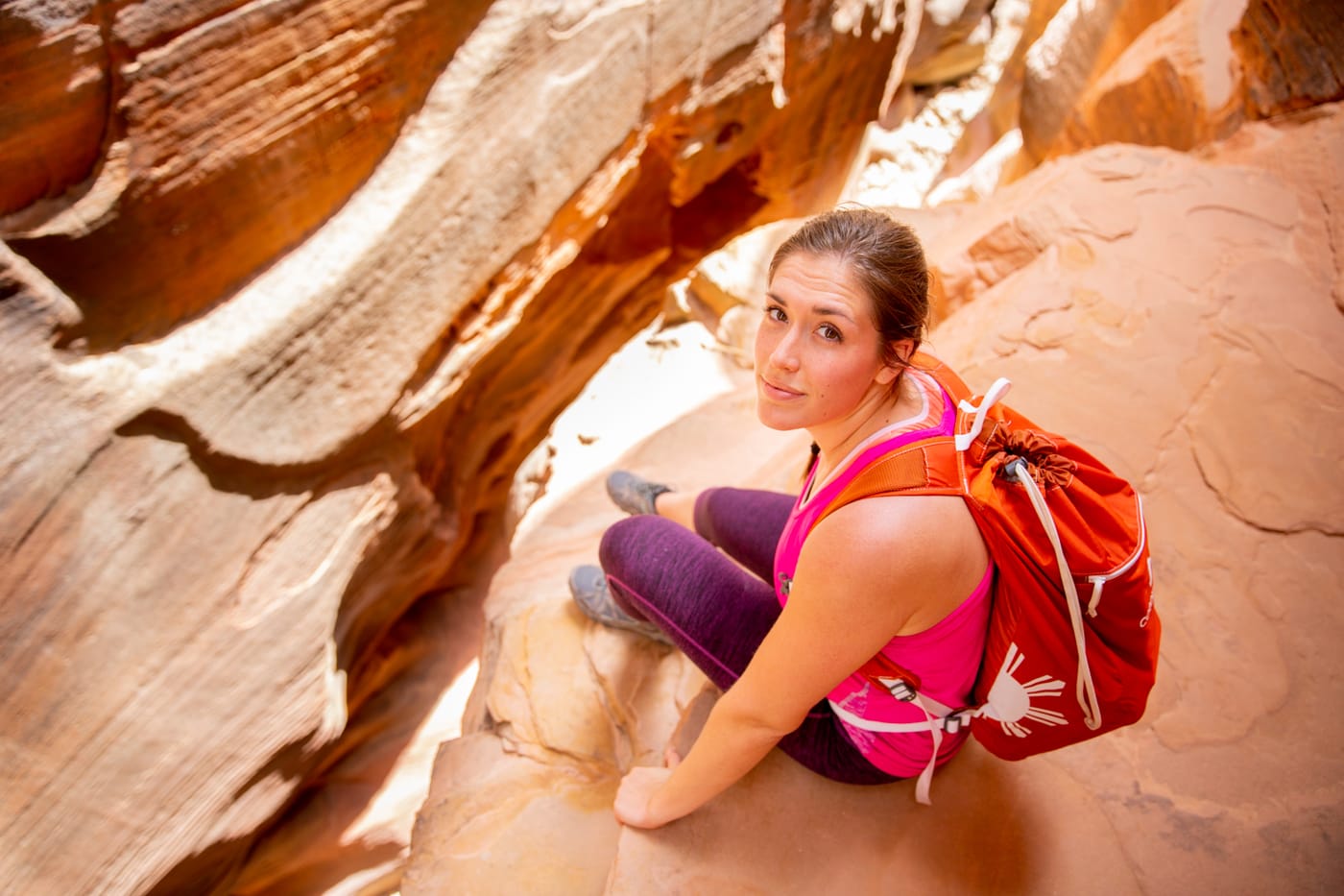 A hiker with a bright pack resting in a sandstone slot canyon