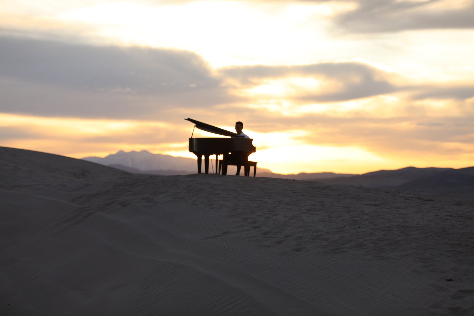 A grand piano silhouetted on sand dunes at sunset