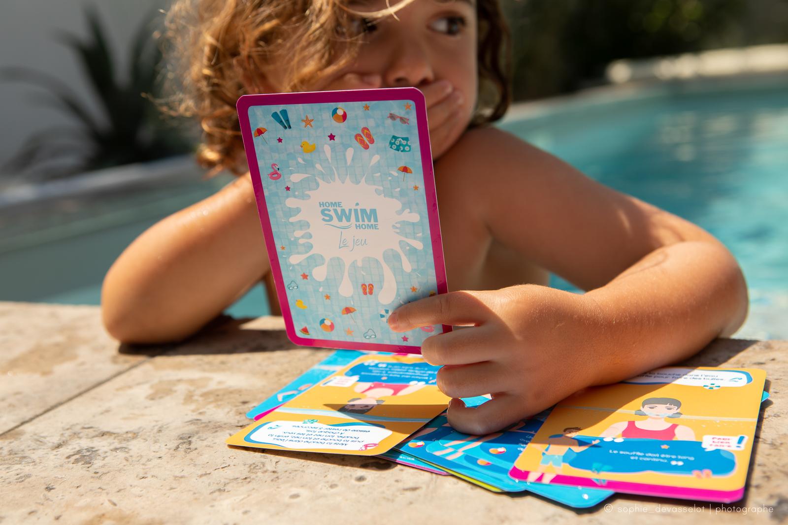 Un enfant accoudé au bord de la piscine joue avec ses cartes