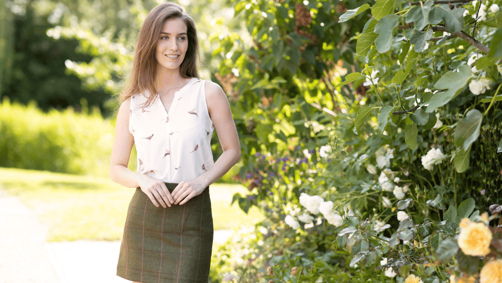 Woman wearing a sleeveless country-print blouse and green tweed skirt in a summer garden.