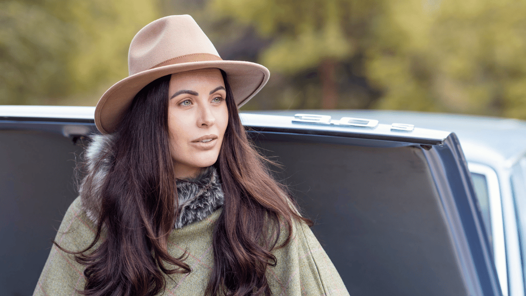 Woman wearing a green tweed cape and neutral felt hat for a winter country wedding.