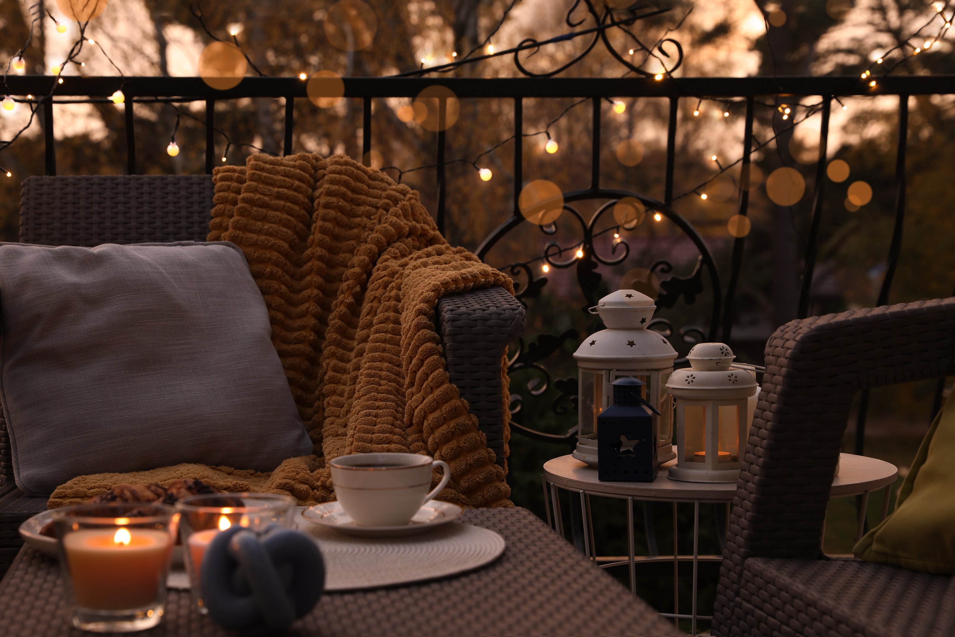 Cosy balcony seating with throws and lanterns, illustrating warm lighting and weatherproof comfort for small outdoor spaces.