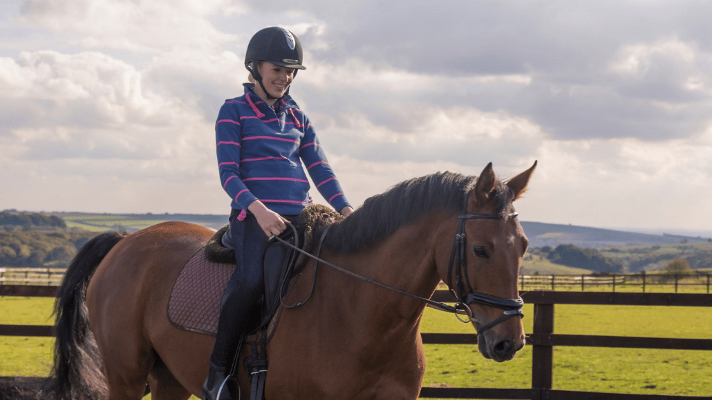 Lady riding a horse through a field.