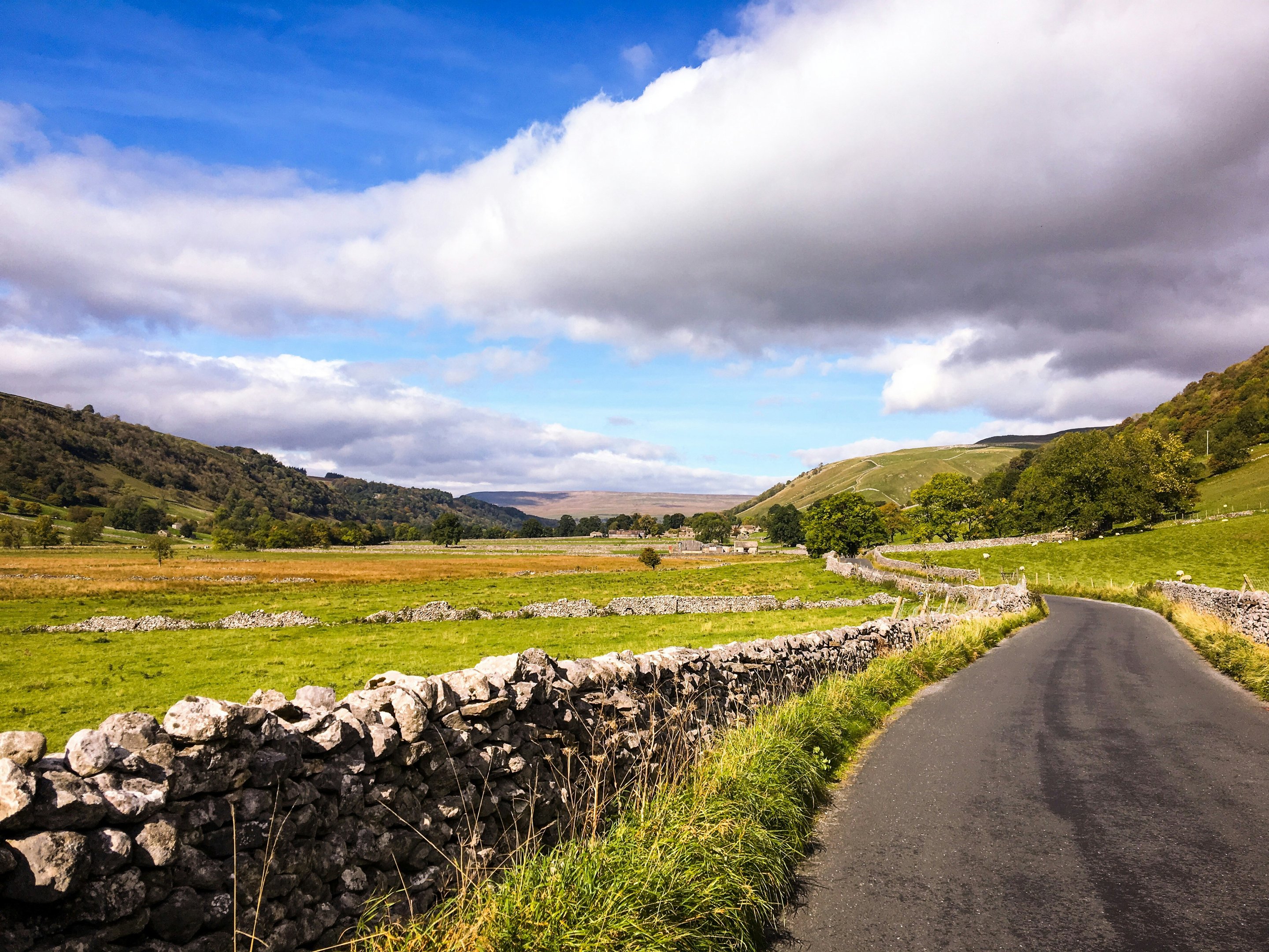 Route de campagne tranquille serpentant à travers les Yorkshire Dales, bordée de murets de pierre, de champs verdoyants et de collines.