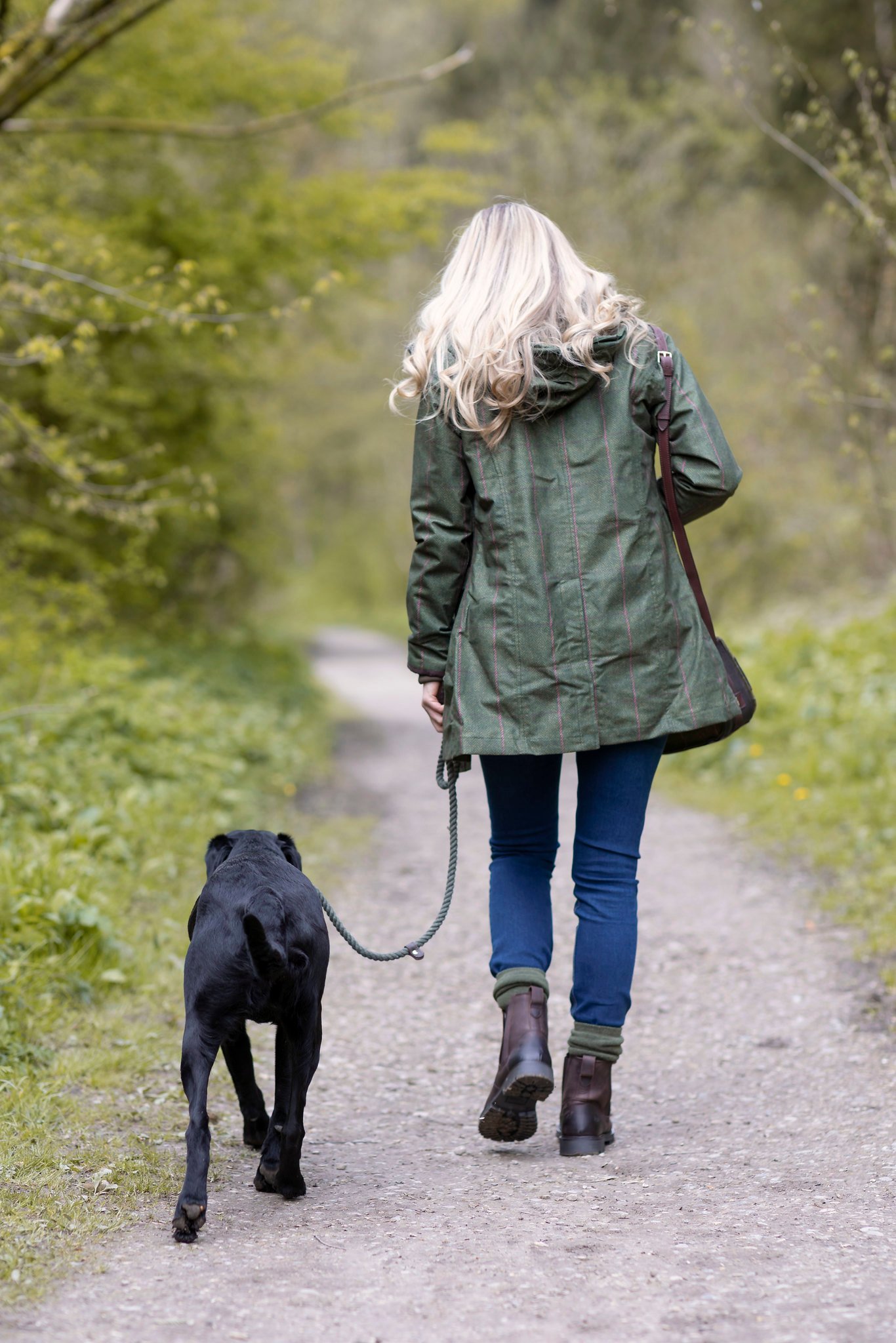 Eine Frau geht mit ihrem an einer Schleppleine geführten Hund durch ein Waldstück.
