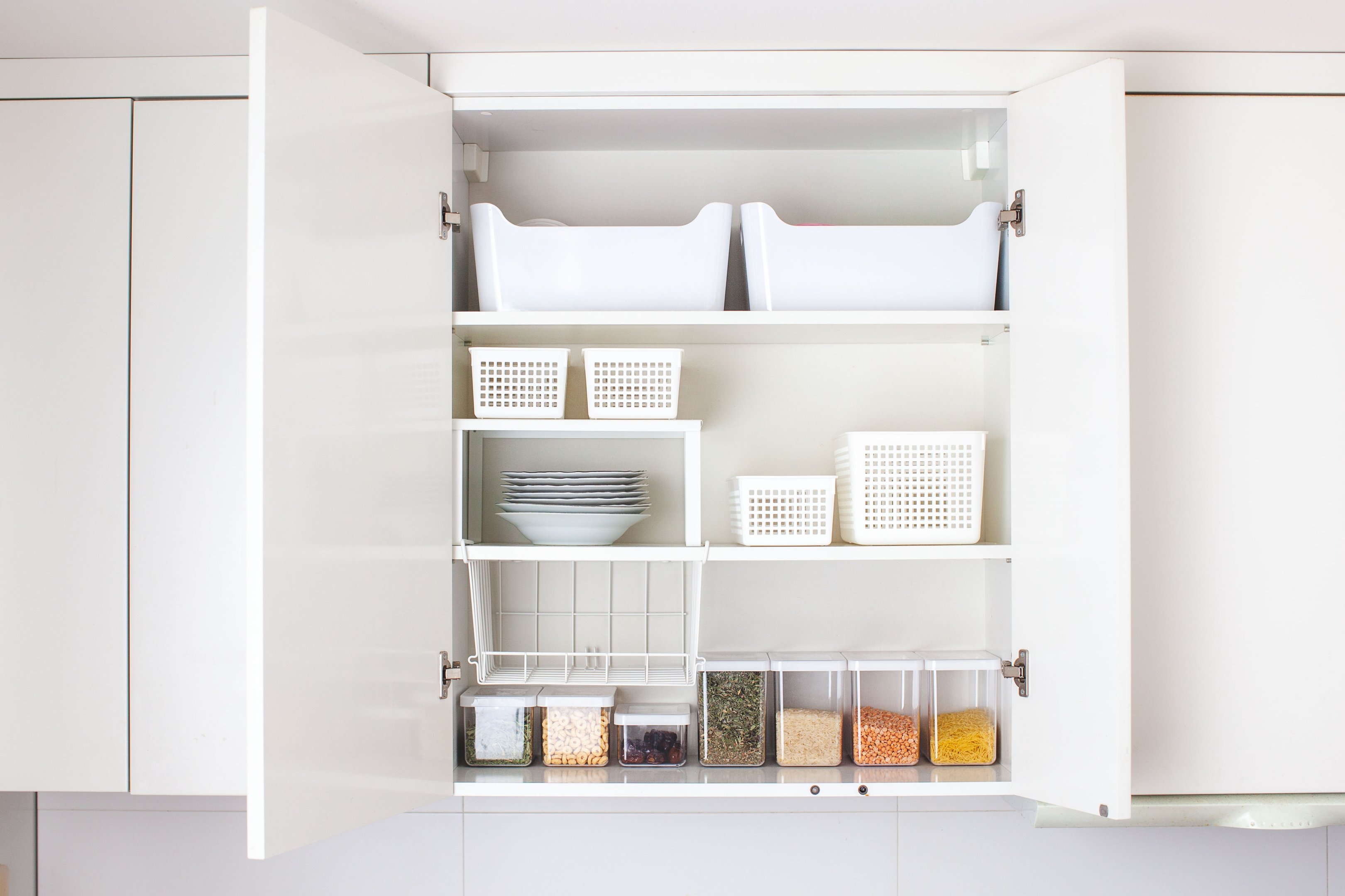 Open kitchen cupboard with storage baskets and clear containers, showing tidy cupboard organisation.