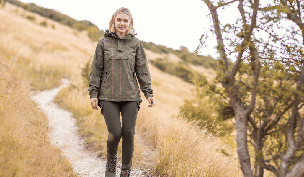 Frau in wasserdichter Country-Jacke, Wanderhose und Wanderschuhen auf einem ländlichen Wanderweg