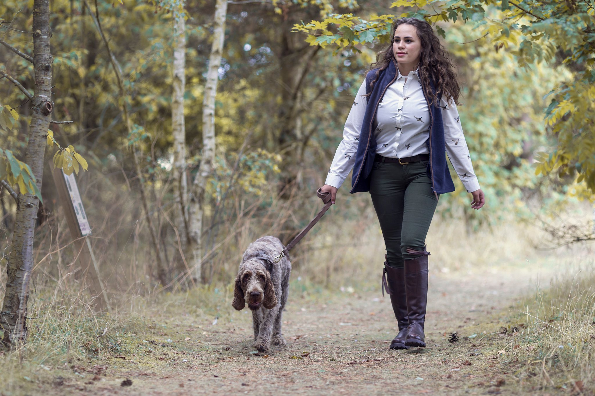 Una mujer pasea a su perro en el bosque.