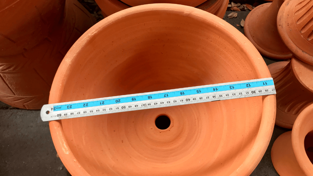 Terracotta plant pot being measured across the top with a ruler to check its diameter.