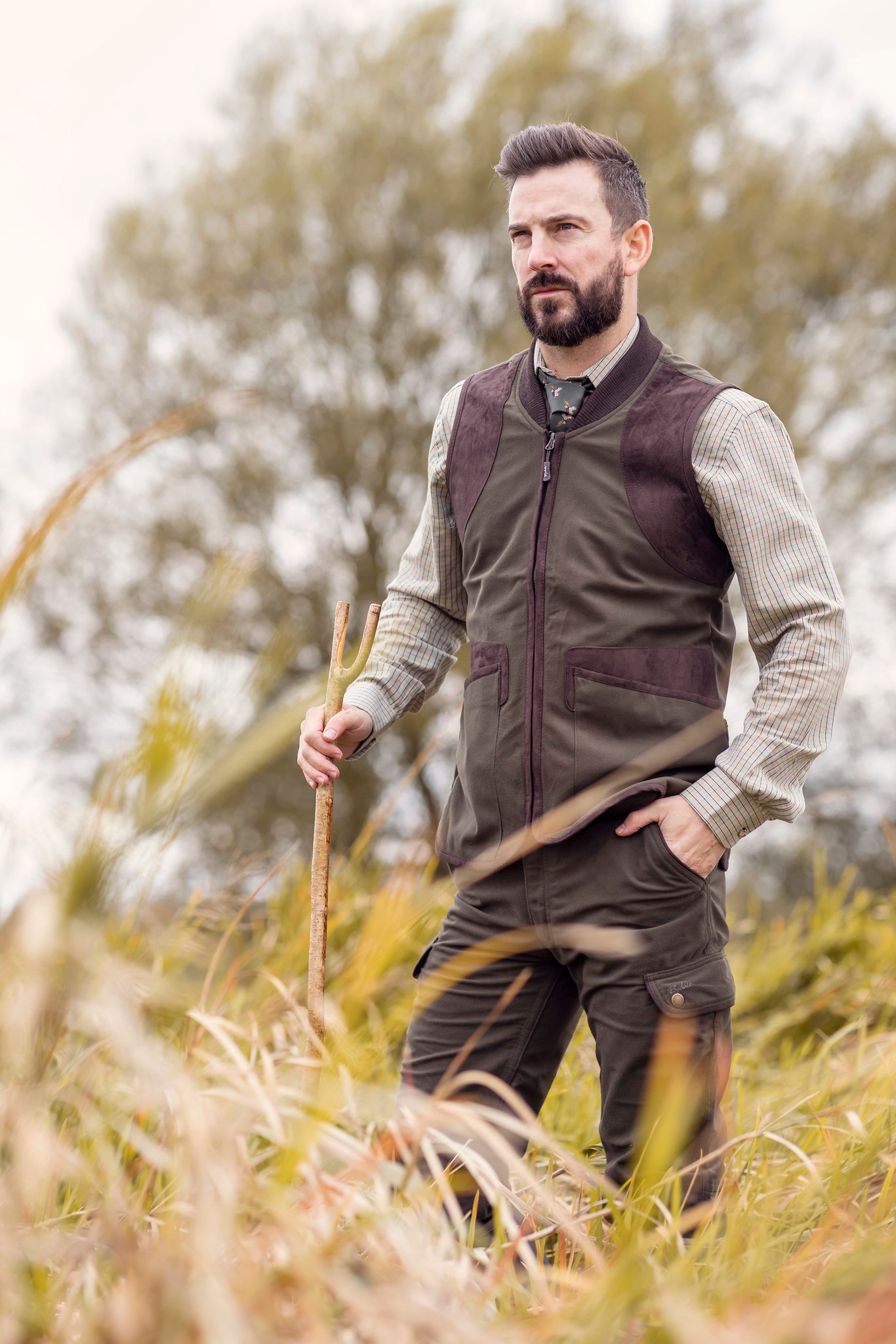 Man wearing a waistcoat and tie with a check shirt in the field.