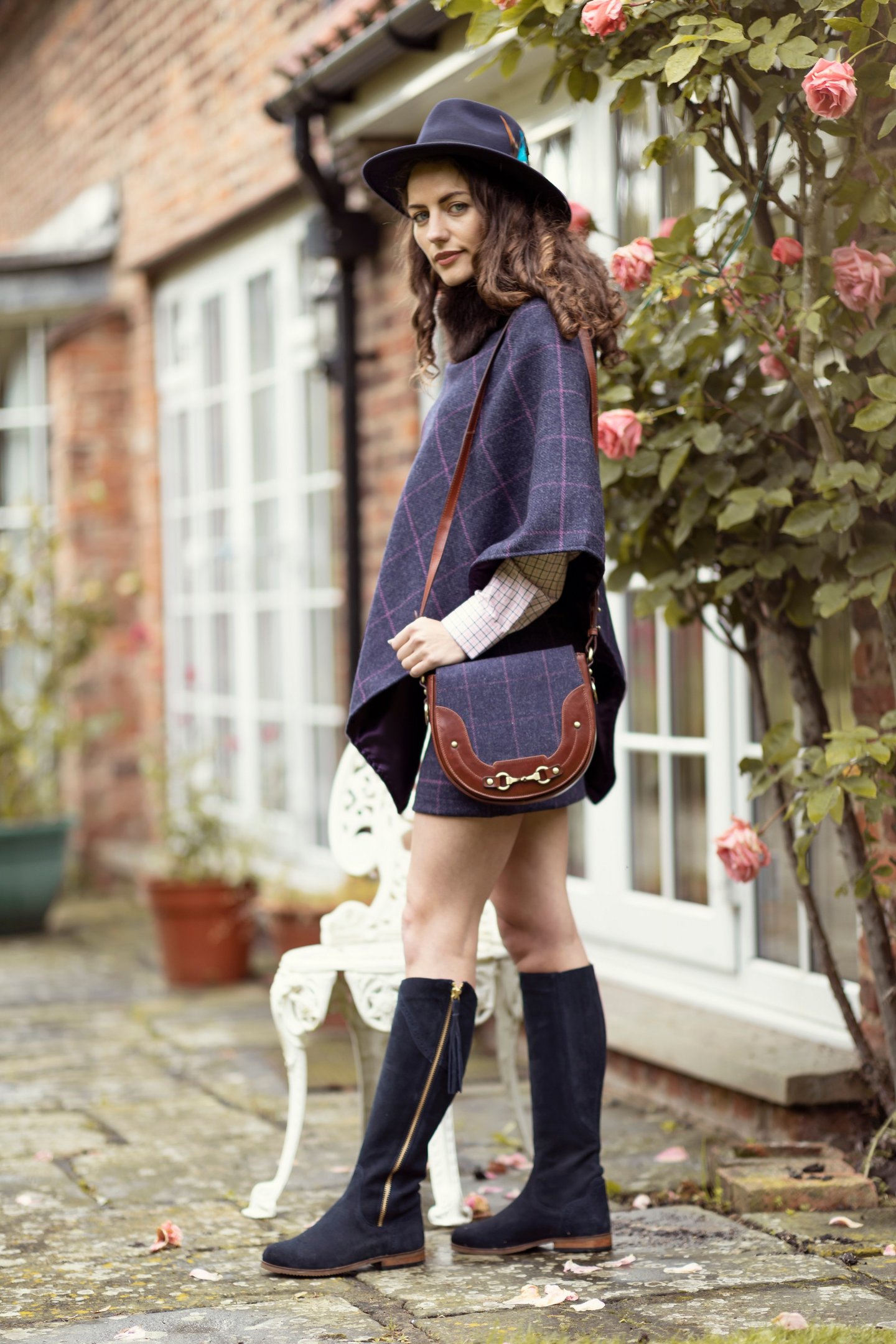 Frau in einem passenden Tweed-Ensemble, Tasche, Panamahut und kniehohen Stiefeln in Marineblau.