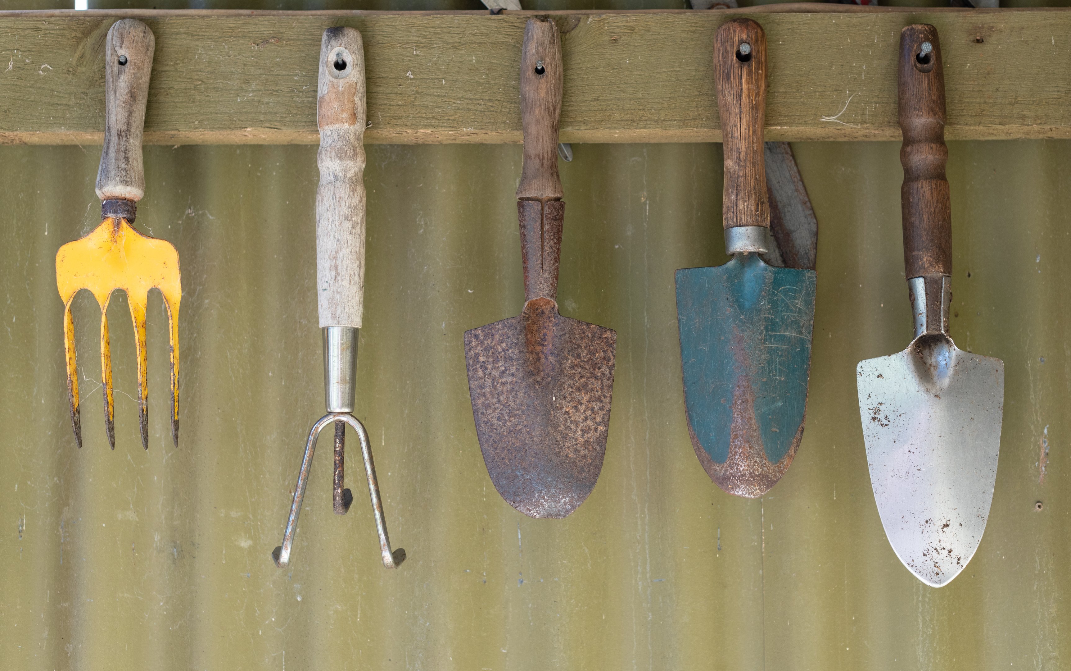 Alt text: Garden hand tools hanging on a wall, showing vertical storage for small patios, courtyards, and balconies.