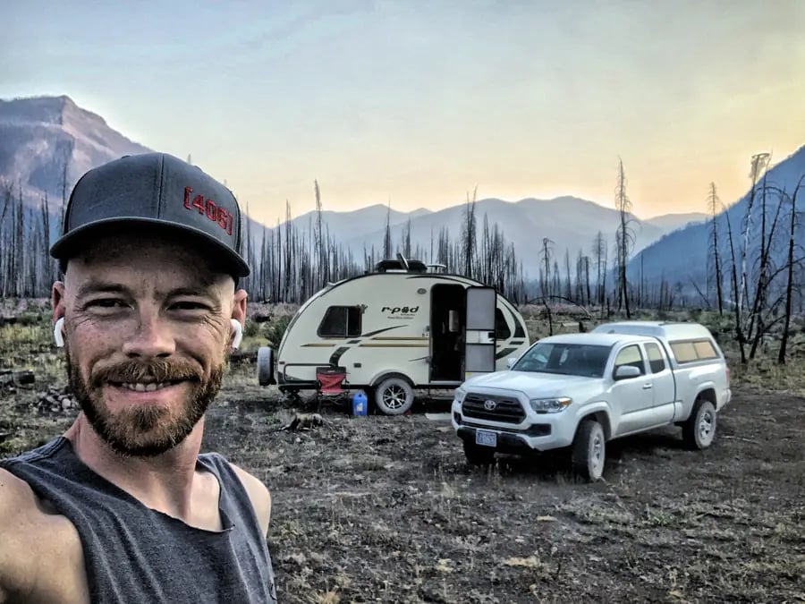 Mark Ulett at a backcountry campsite, Montana mountains and r-pod camper behind him