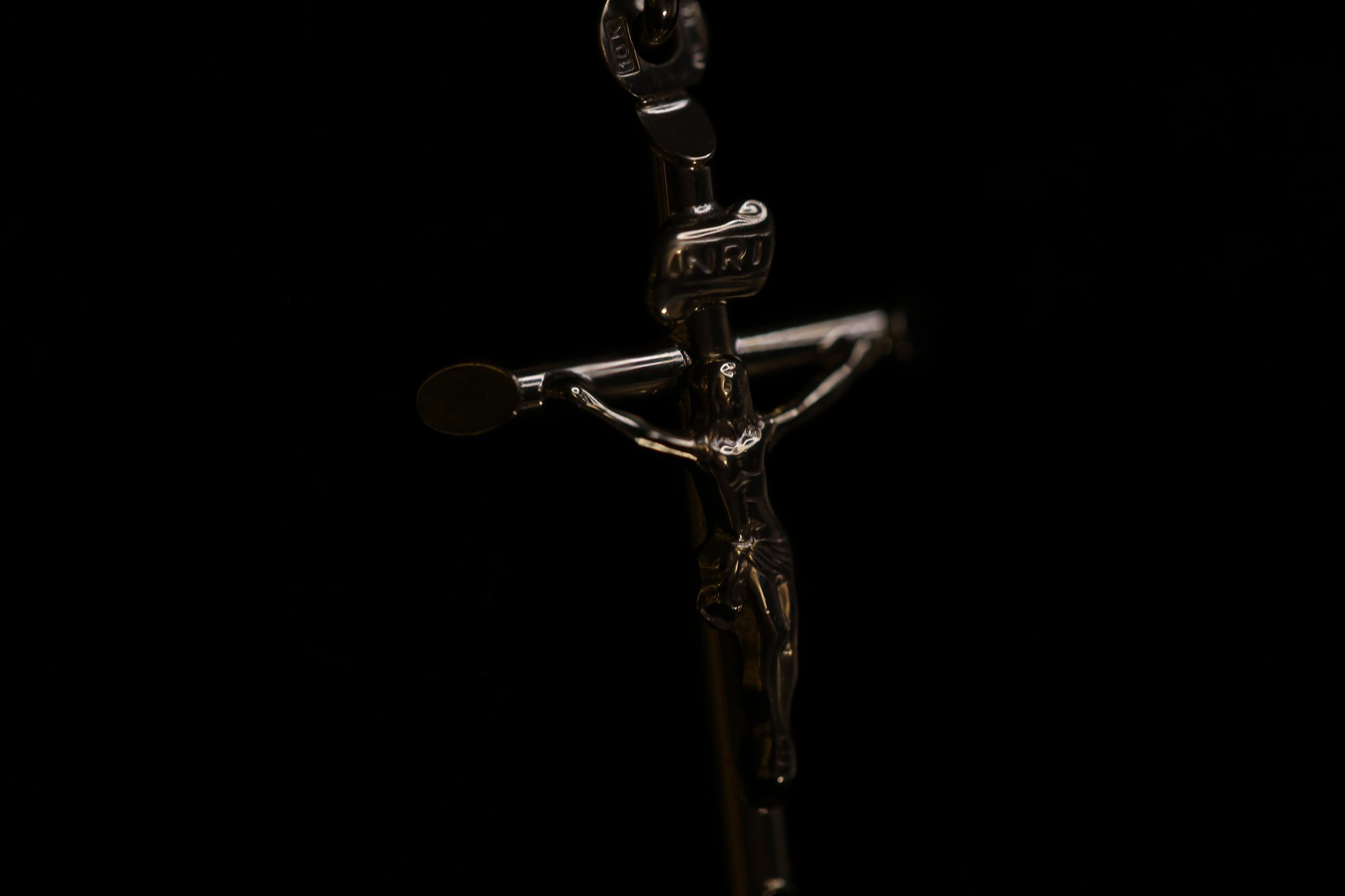 Close-up detail of a silver crucifix pendant showing the corpus figure and INRI tablet inscription at the top of the cross
