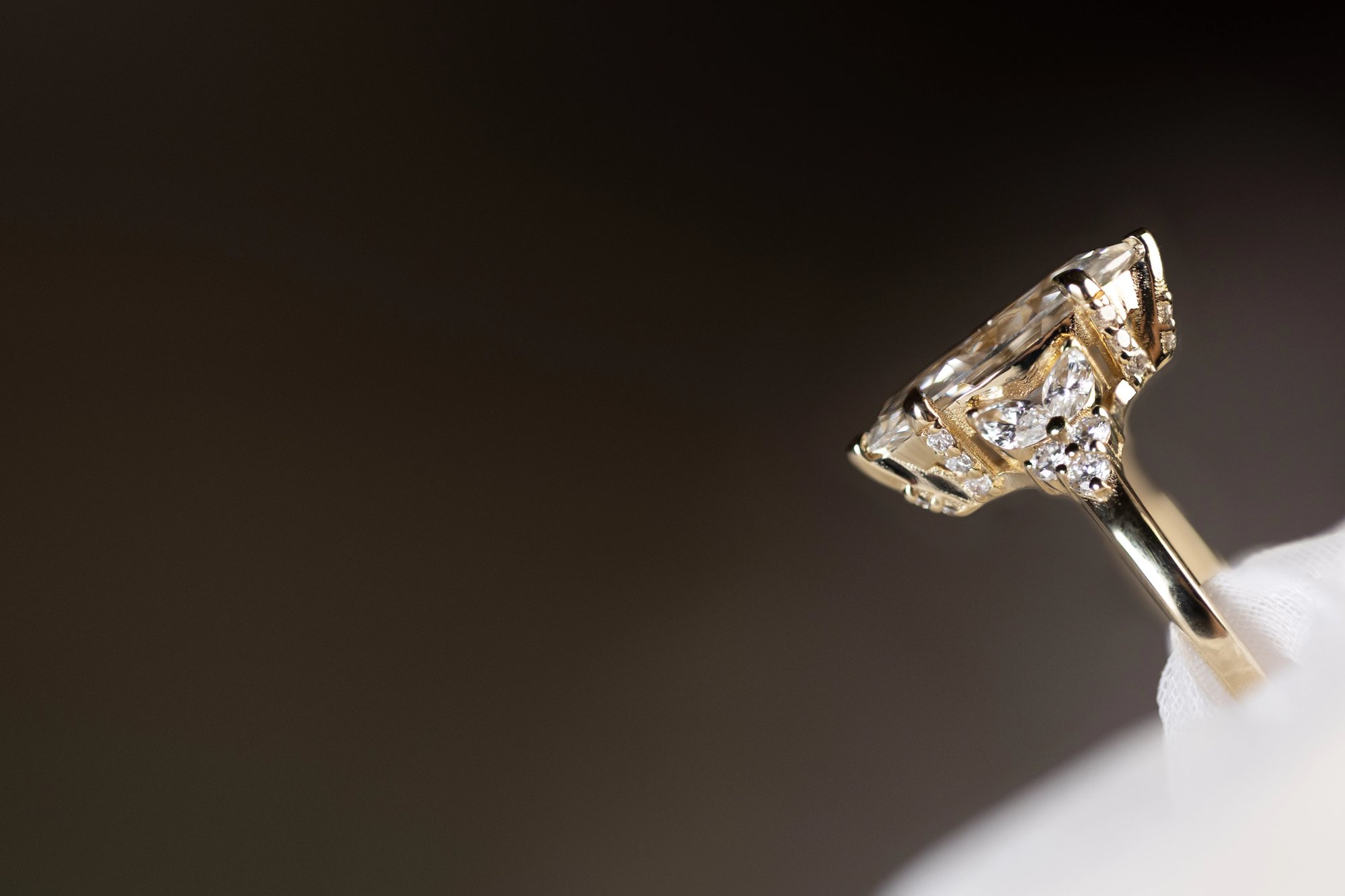 Marquise diamond ring in yellow gold photographed in profile against a dark background, showing the architectural underside of the setting and the faceted marquise stone from the side