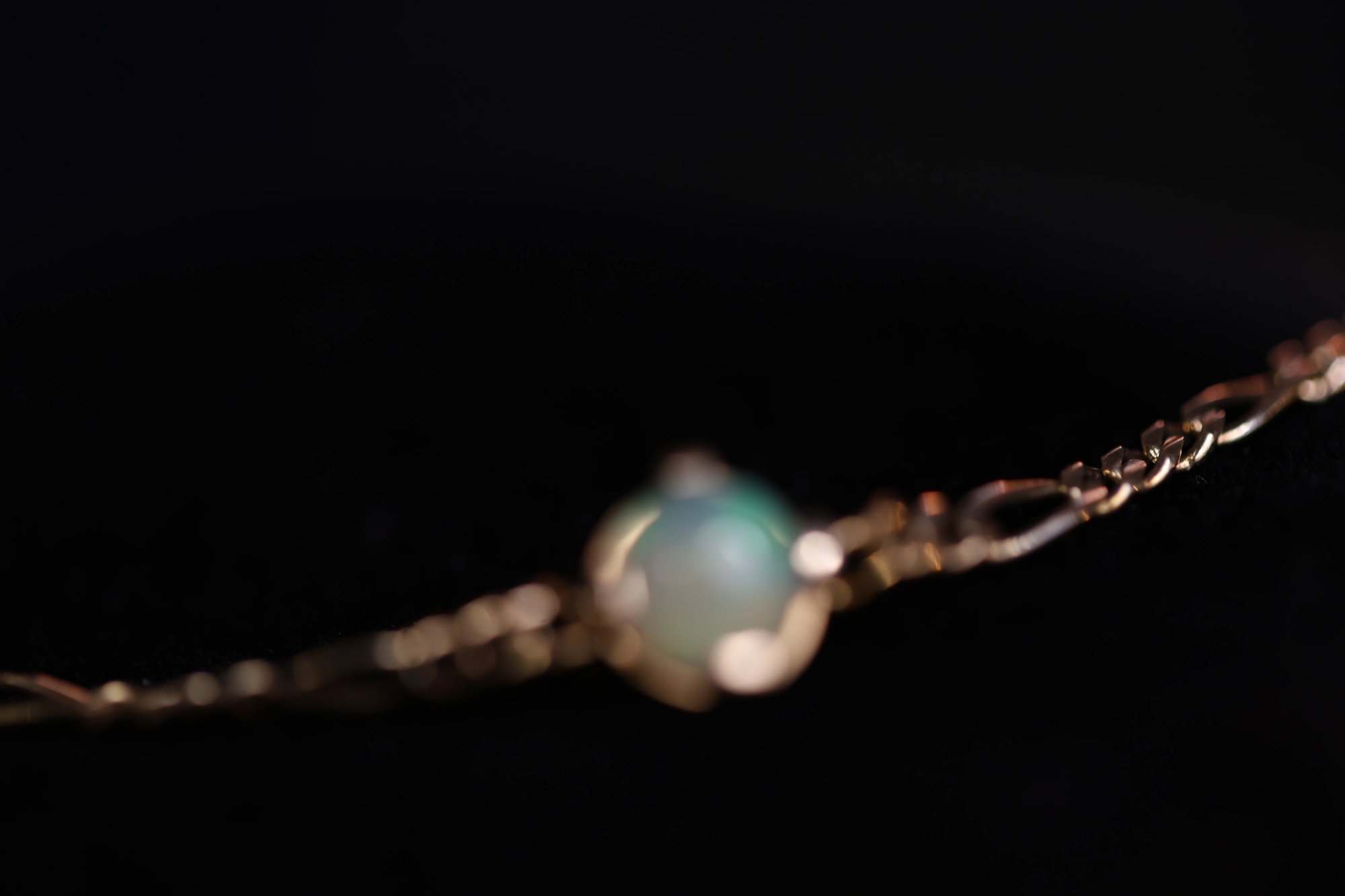 Opal bracelet suspended against a black background with the round cabochon stone showing faint blue-green iridescence in a gold setting