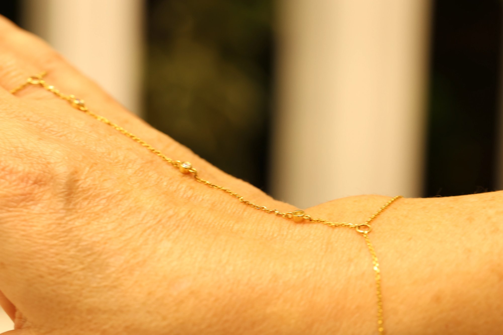 Close-up of a fine yellow gold hand chain worn across the back of the hand, showing the delicate chain strands and bezel-set diamond stations in detail