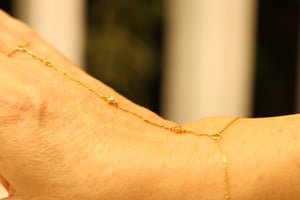 Close-up of a fine yellow gold hand chain worn across the back of the hand, showing the delicate chain strands and bezel-set diamond stations in detail