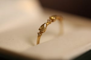 Yellow diamond ring in yellow gold resting in a white-lined jewelry box, showing the pear-cut yellow diamond center stone and delicate band with white diamond accents from a low side angle