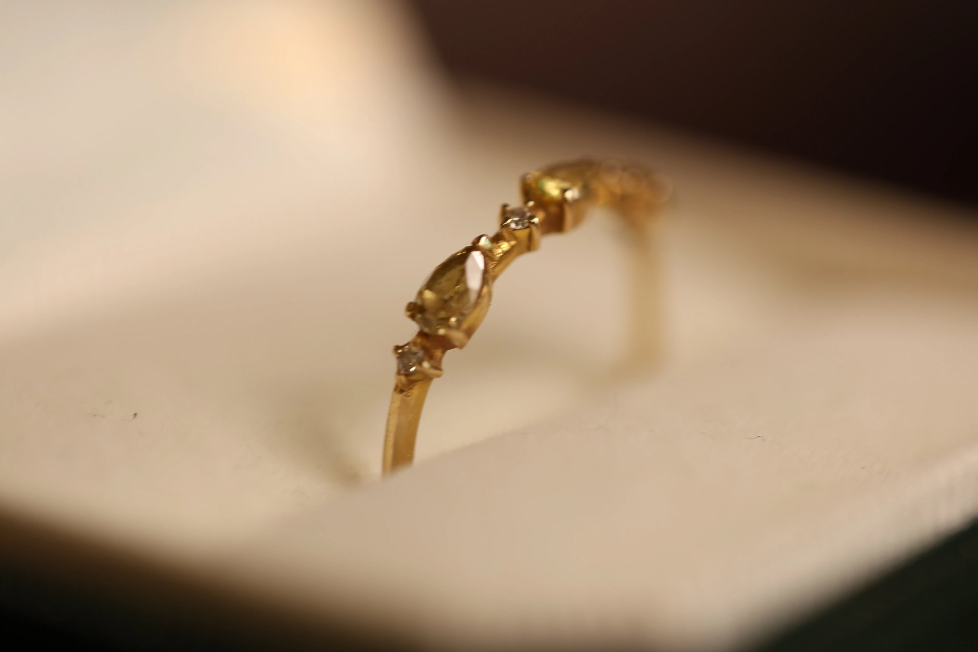 Yellow diamond ring in yellow gold standing upright in a white-lined jewelry box, showing a pear-cut yellow diamond center stone with small round white diamond accents on either side of the delicate band