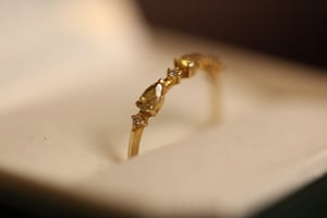 Yellow diamond ring in yellow gold standing upright in a white-lined jewelry box, showing a pear-cut yellow diamond center stone with small round white diamond accents on either side of the delicate band