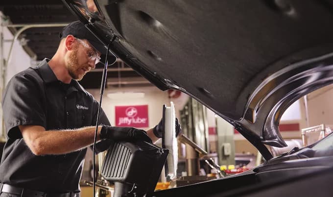 Jiffy Lube technician replacing a vehicle air filter under the hood