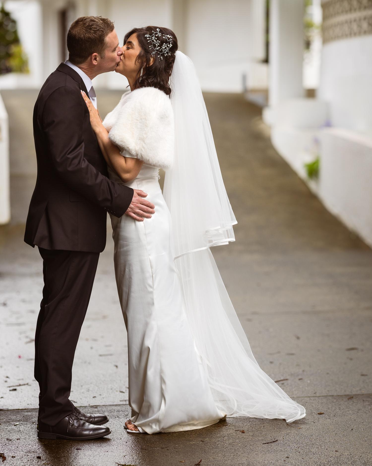Feby and Steven kiss on the covered walkway at The Waitākere Resort and Spa