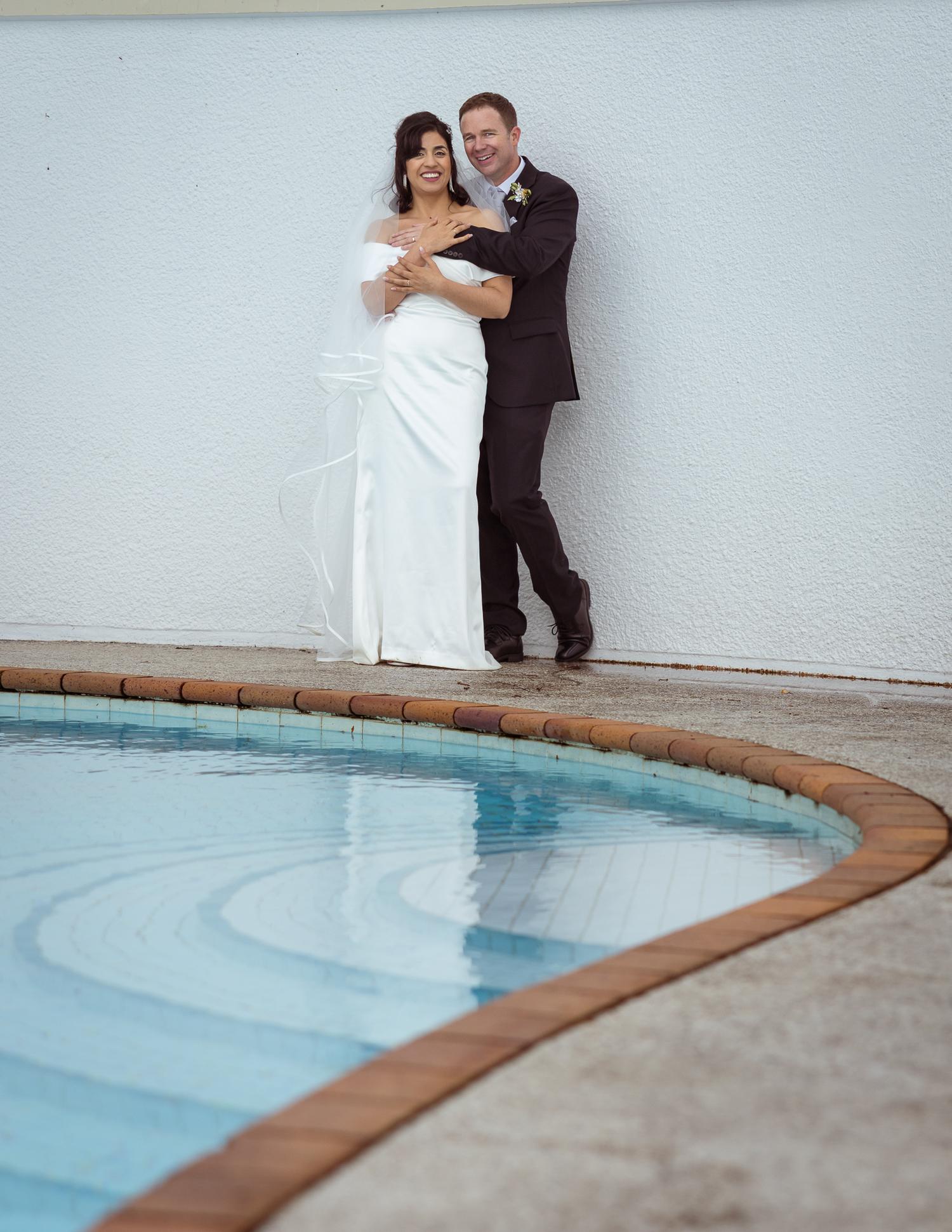 Feby and Steven lean against a white wall by the pool