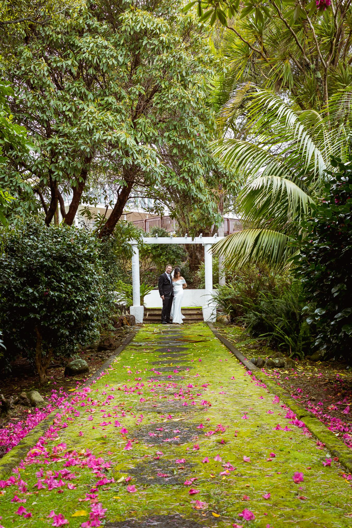 A moss-covered path scattered with pink petals leading to a white arbour