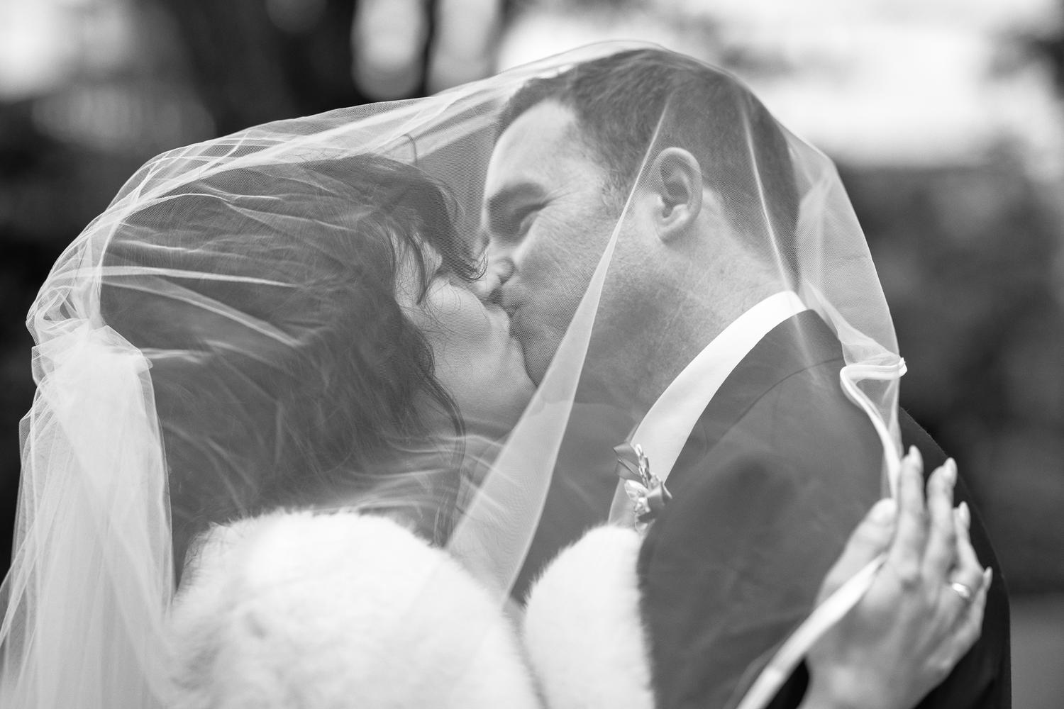 Black and white photo of Feby and Steven kissing under her veil