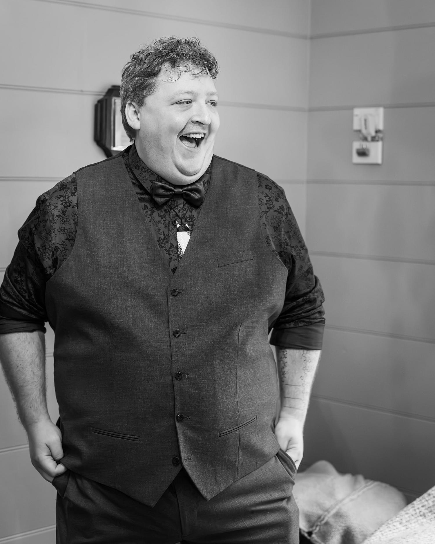 A guest in a black vest and bow tie is laughing and smiling