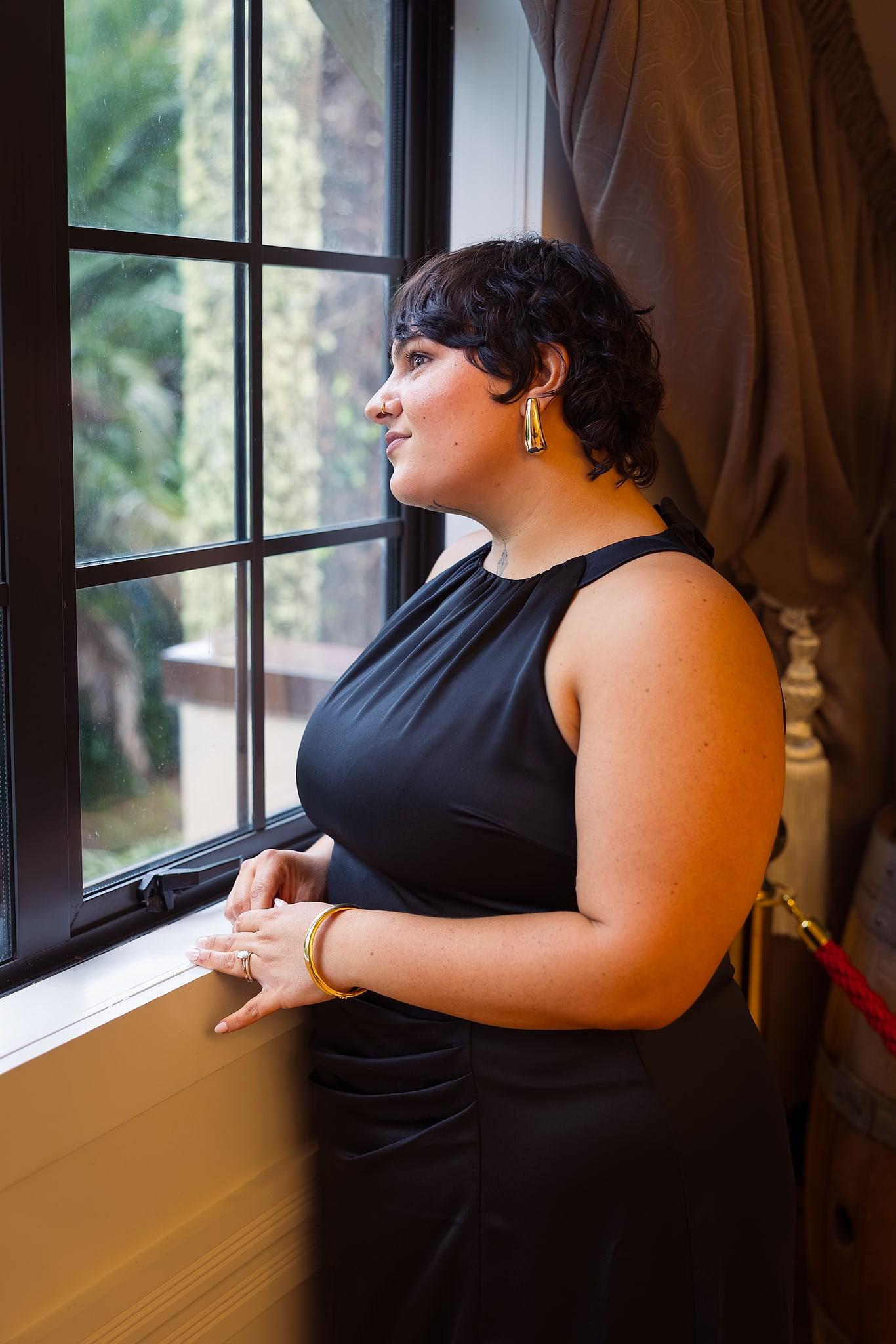 A woman in a black dress looks out the window