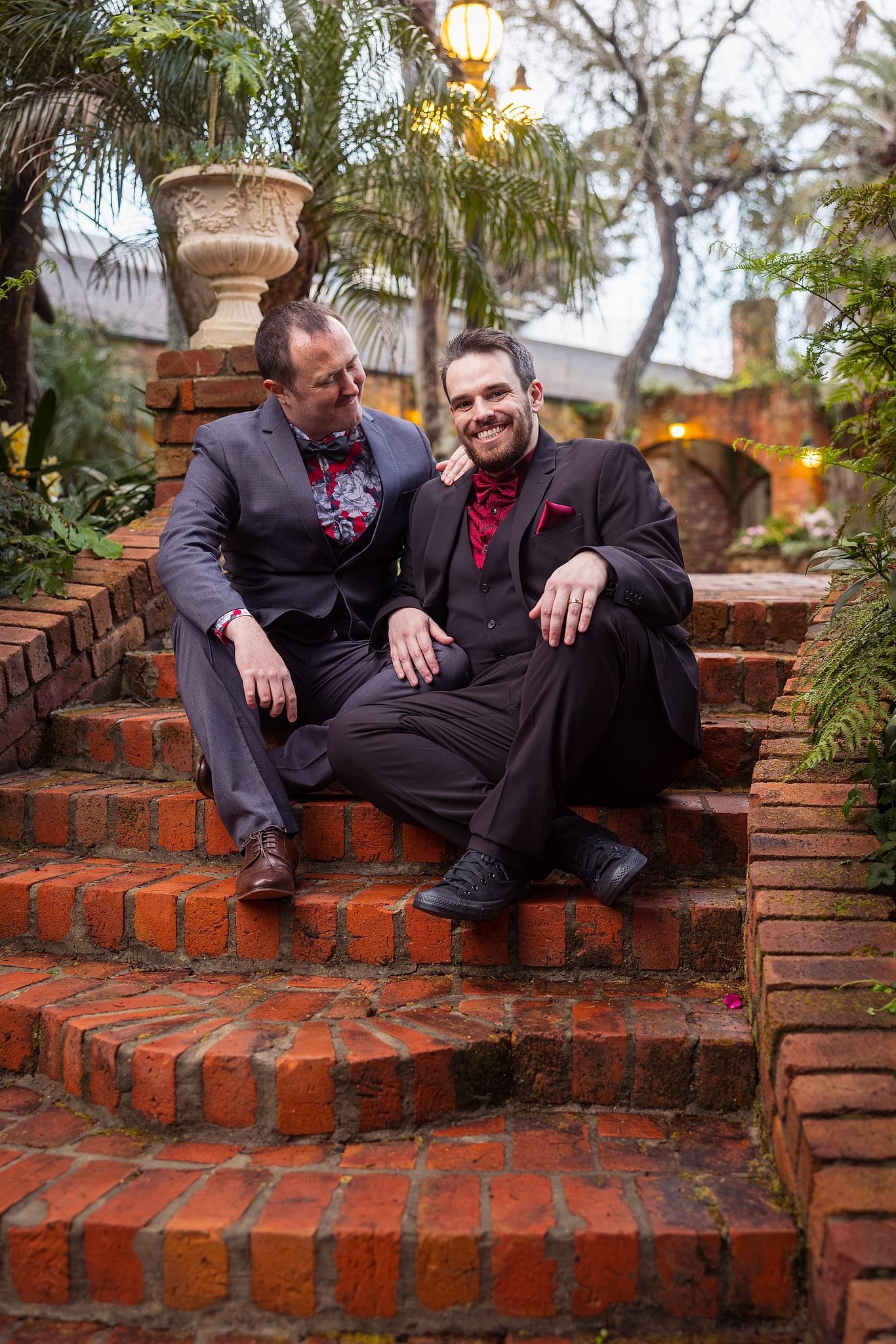 Two men, Josh and Paul, are sitting on a brick staircase, wearing suits and ties