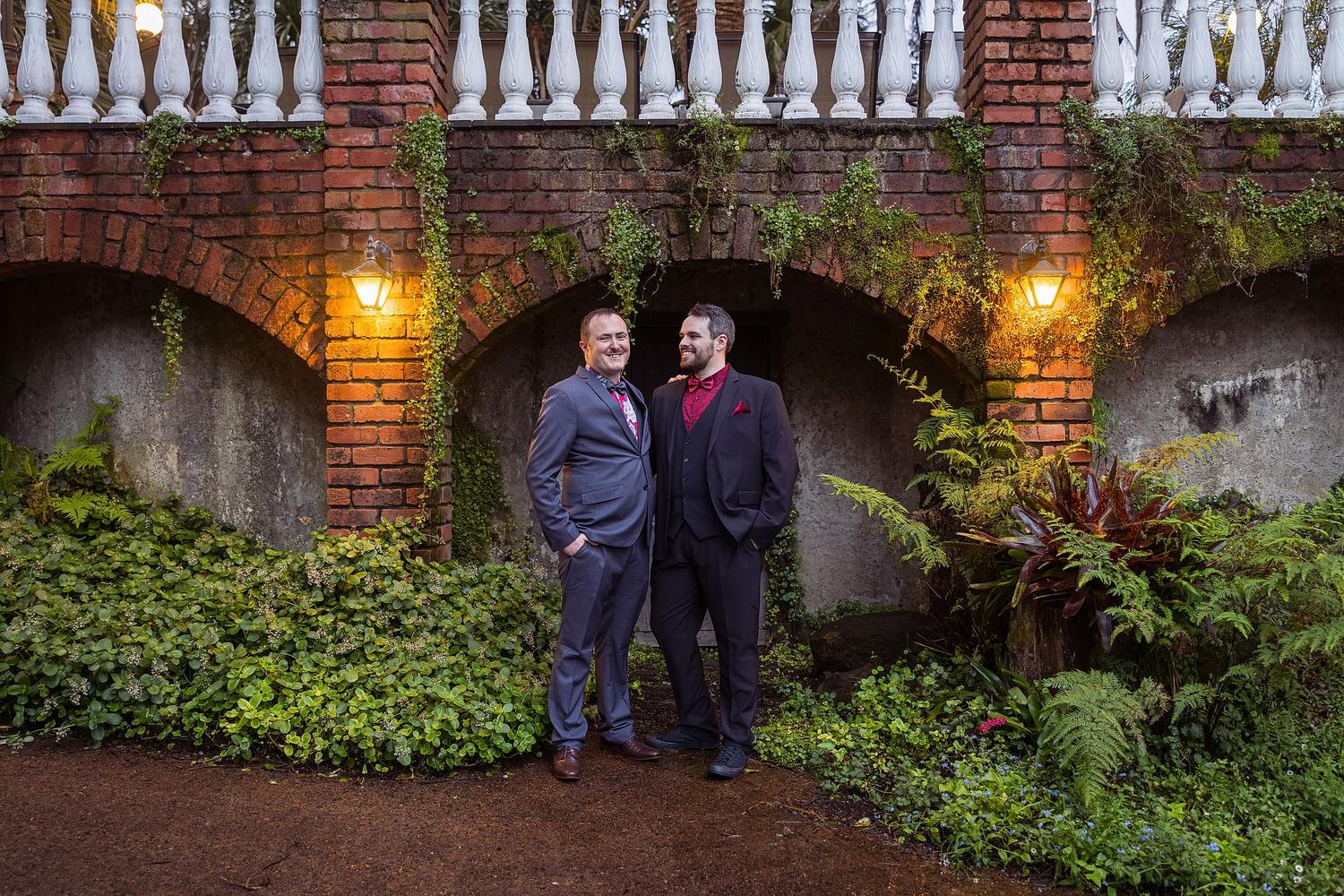Josh and Paul, pose for a wedding photo in front of a brick building