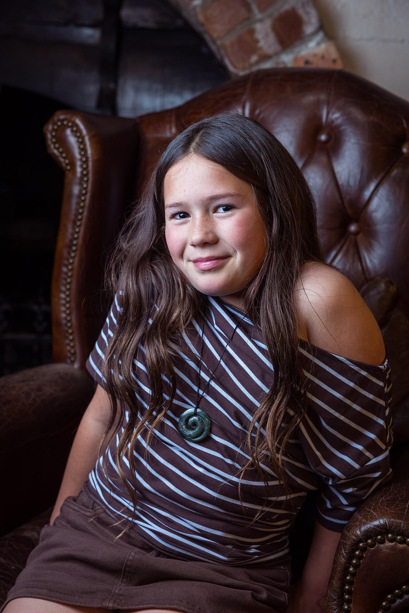 A young girl wearing a striped shirt sits in a chair