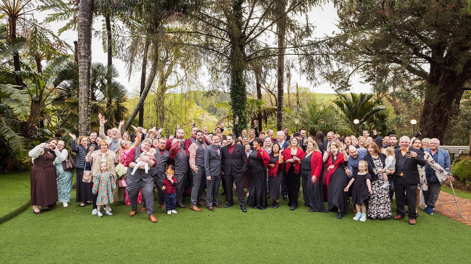 A group of people, including Josh and Paul, pose for a wedding photo in front of a tree