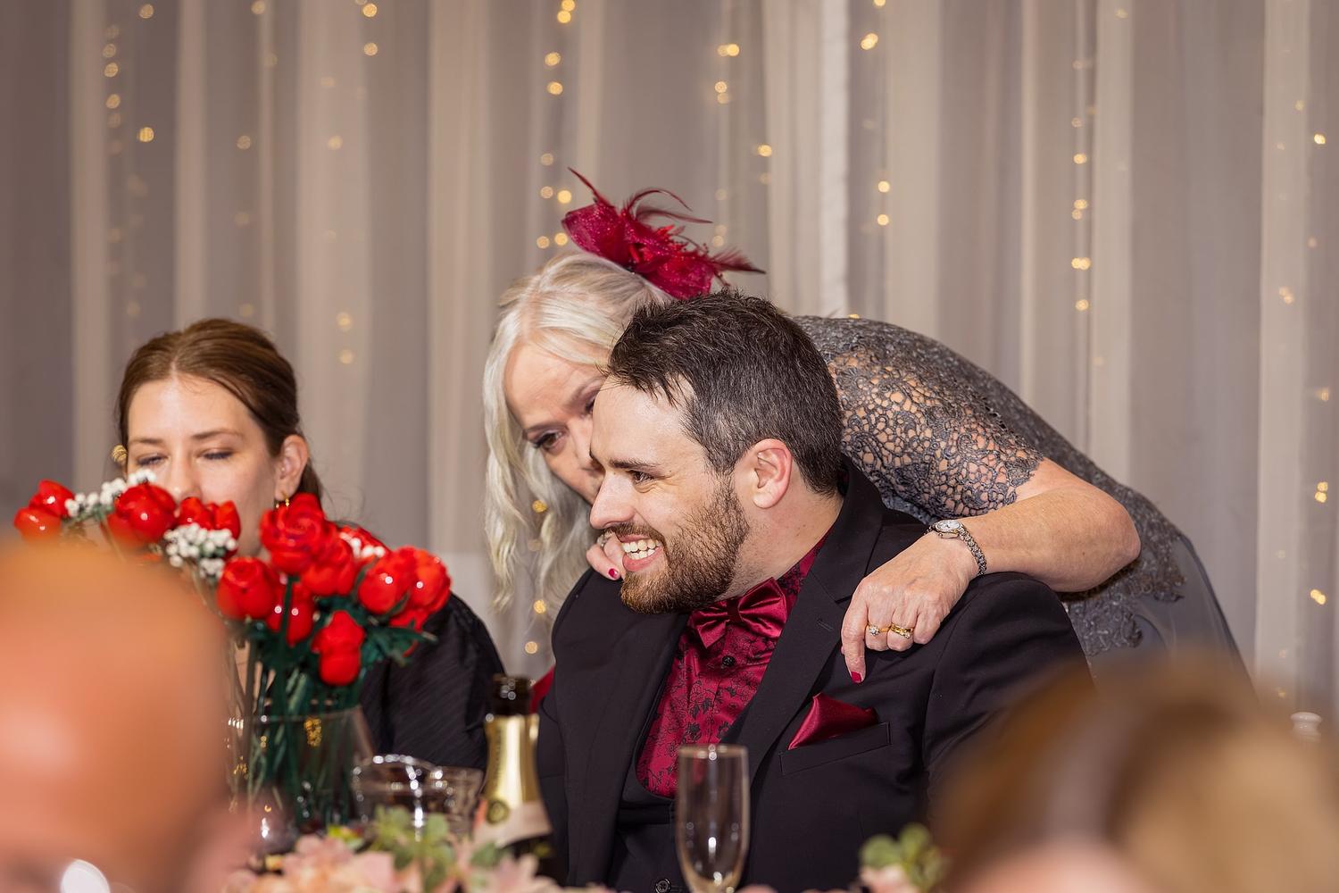 A woman is leaning over a man in a tuxedo, smiling and laughing