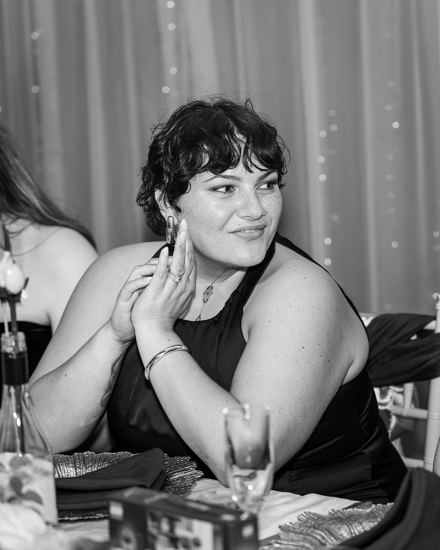 A woman in a black dress is sitting at a table with a wine glass in front of her