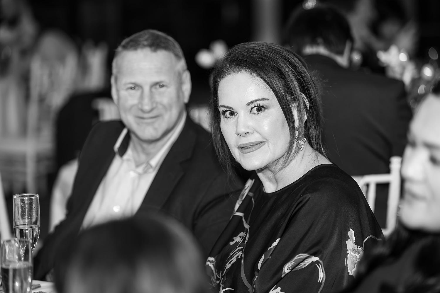 A man and woman are sitting at a table, smiling for the camera
