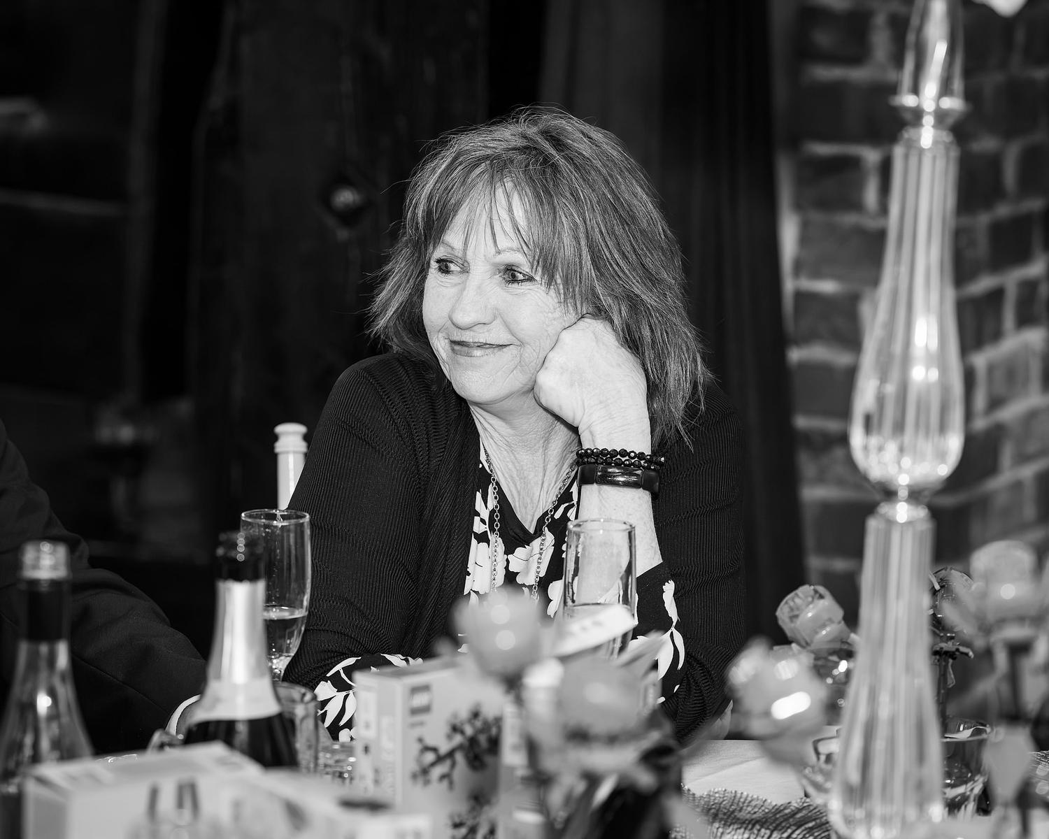 A woman with long hair and a black shirt is sitting at a table with wine glasses and a bottle of wine