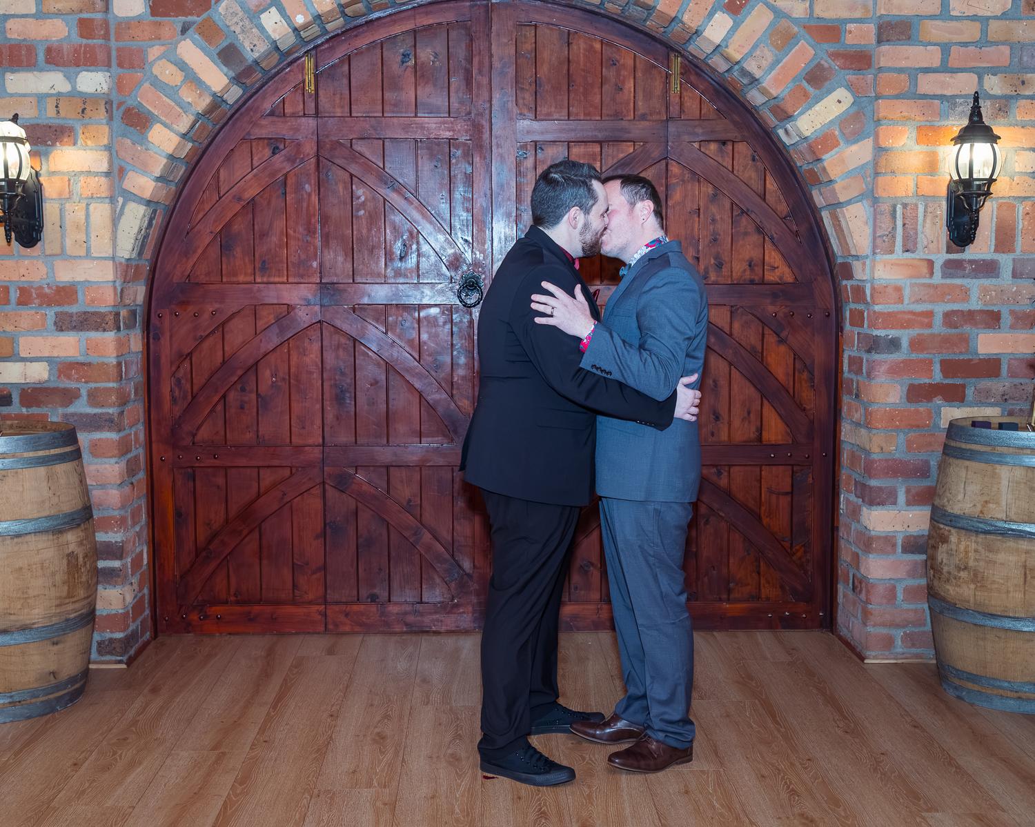 Josh and Paul kiss in front of a wooden door