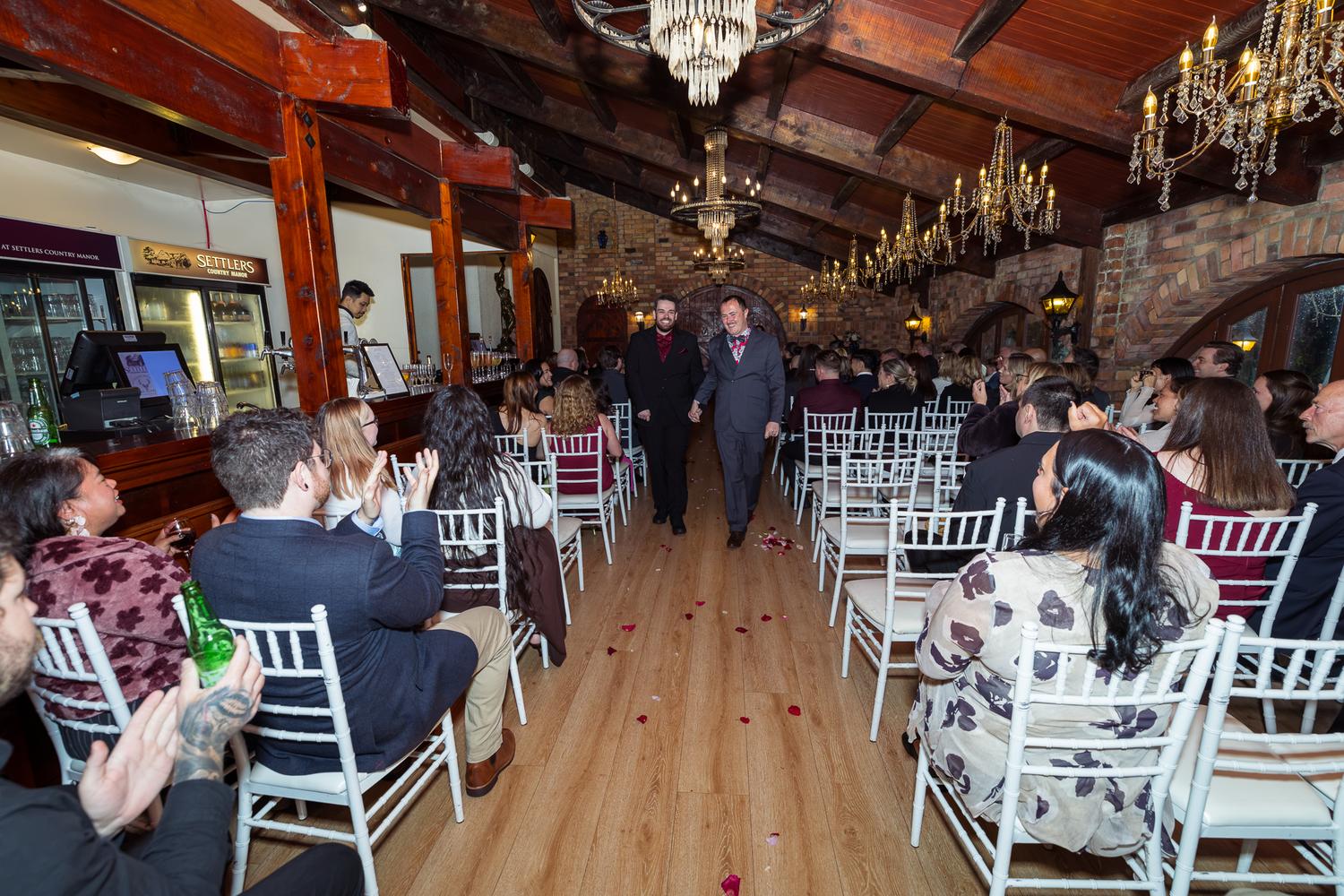 Josh and Paul walk back down the aisle as their guests clap and cheer